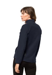 Marineblauwe fleecejas met een hoge kraag, een zachte textuur, zijzakken en een discreet logo-label vlakbij de zoom. Lichtgewicht en getailleerd ontwerp.