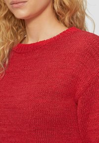 Roter gestrickter Pullover mit rundem Halsausschnitt, strukturiertem Muster und gerippten Akzenten am Halsausschnitt und an den Ärmelöffnungen.