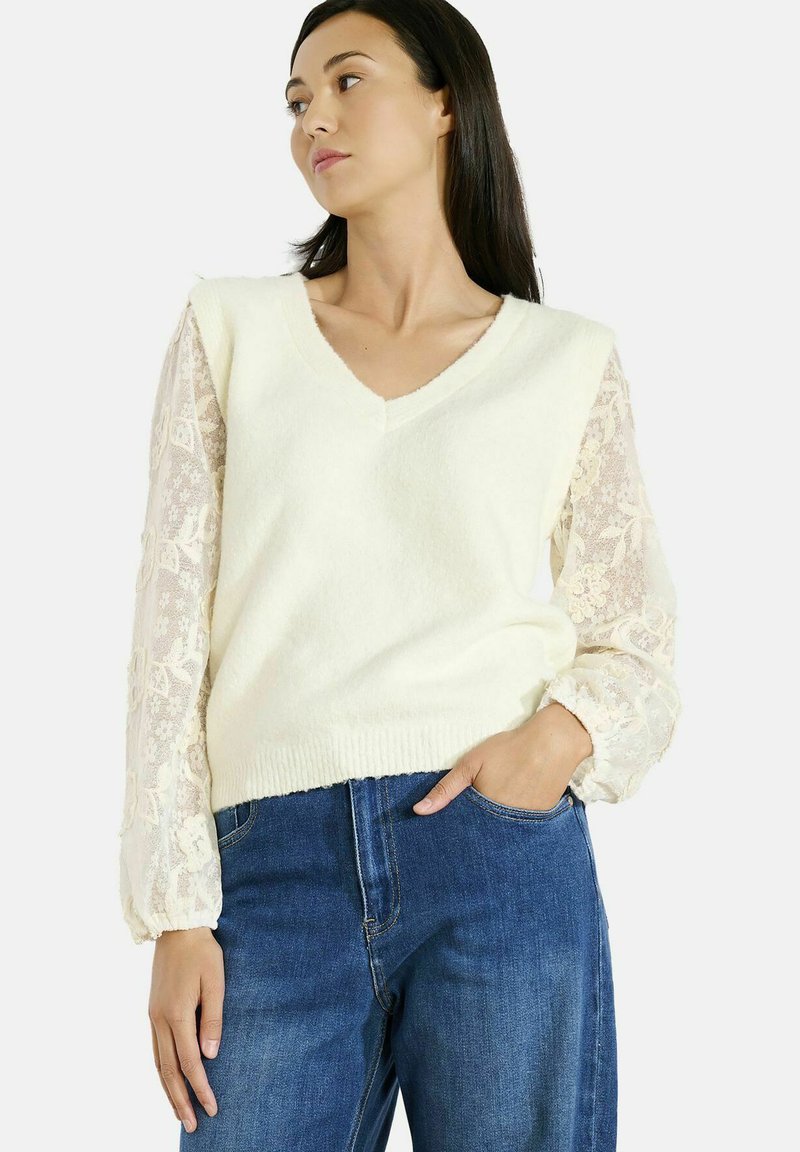 Maglione a v con corpo lavorato a trama e maniche lunghe in pizzo trasparente. Abbinato a jeans blu. Tessuto morbido con bordo e polsini a coste.