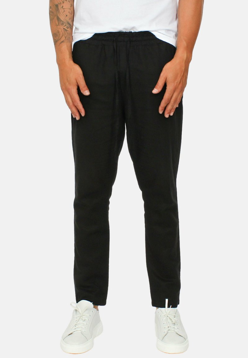 Pantaloni neri a sigaretta con elastico in vita, realizzati in tessuto leggero, abbinati a sneakers bianche. Texture liscia, design minimal.