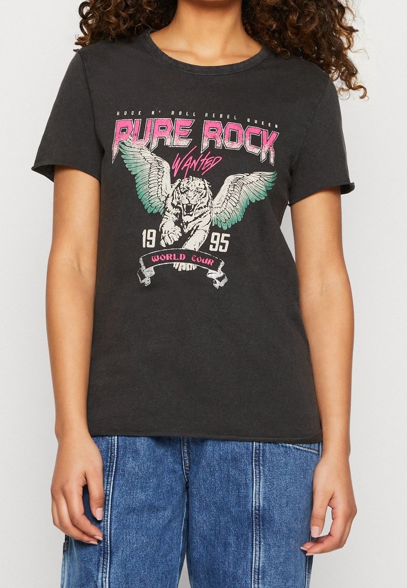 T-shirt noir avec motif de tigre ailé et le texte "Pure Rock Wanted 1995 World Tour,", porté par une personne en jean bleu.