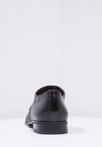 Chaussure habillée en cuir noir avec une surface texturée, un bout arrondi et une semelle extérieure profilée. Présente des accents lisses au niveau du talon et du col.