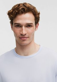 Heldblauw, T-shirt met korte mouwen en ronde hals, gemaakt van een gladde, gestructureerde stof, gedragen door een persoon met kort golvend haar.