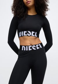Czarna krótka bluzka z długim rękawem i wysokim stanem legginsy z widocznym białym logo "DIESEL" na taśmie, gładka faktura i dopasowany krój.