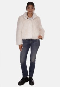 Giacca corta in pelliccia sintetica di colore rosa chiaro, con colletto alto e bottone dorato, abbinata a jeans blu scuro e stivali neri stringati.