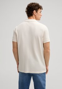 Beige polohemd met korte mouwen, van getextureerd katoen en een klassieke kraag. Zijsplitten zichtbaar aan de zoom voor extra comfort.
