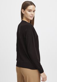 Schwarzer Strickpullover mit lockerer Passform, langen Ärmeln und gerippten Bündchen. Glatte Textur, runder Ausschnitt und leicht längerer hinterer Saum.