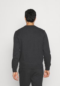 Mörkgrå crewneck sweatshirt, tillverkad av texturerat tyg. Har ribbade muddaroch fåll samt en enkel design. Bärs med matchande joggers.