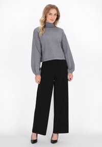 Grauer, hochtaillierter, kurzer Pullover mit Ballonärmeln, kombiniert mit schwarzen, weit geschnittenen Hosen und schwarzen Absätzen. Glatte Texturen und schlichtes Design.