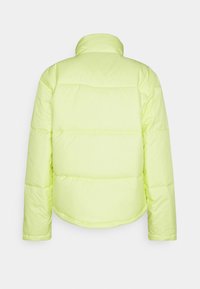 Uppblåst jacka i stark neon-gul, med ståkrage och horisontell sömnad. Manschetterna och fållen är elastiska för en tät passform.