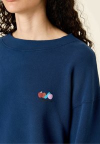 Felpa blu navy con colletto arrotondato e design ricamato di frutta in rosso, azzurro chiaro e rosa sul lato sinistro del petto. Texture morbida.