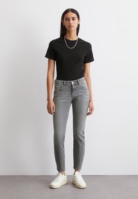 Chemise noire à rayures et à manches courtes, jeans gris slim et baskets blanches ; design simple avec une texture lisse et une silhouette classique.