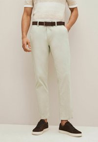 Chinos vert clair avec une coupe droite, dotés d'une fermeture éclair à l'avant, de poches latérales et d'une ceinture en cuir marron. Portés avec des baskets marron foncé.