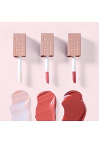 Drie lipgloss-tubes in beige verpakking met een witte applicator. Hieronder zijn swatches in lichtroze, zachtroze en donkeren rode tinten.