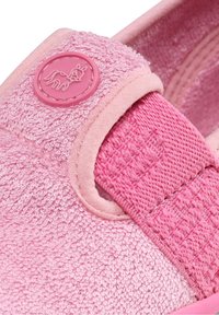 Nærbillede af en pink børnesko med frottéstruktur, elastisk rem og hestemblem på remmen.