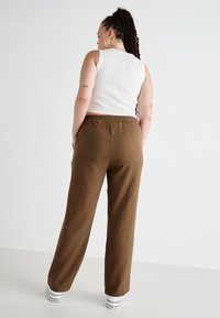 Brown pinstriped trousers with an elastic waistband, paired with a sleeveless white top, and white sneakers; viewed from the back.