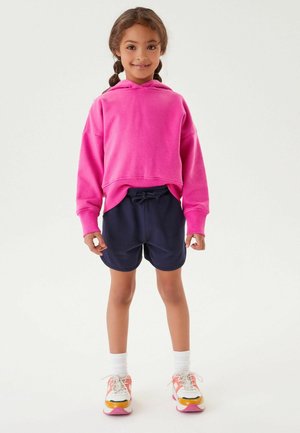Felpa con cappuccio rosa, pantaloni shorts blu scuro, calze bianche e scarpe multicolori. Materiali morbidi e casual con una vestibilità rilassata e coulisse.