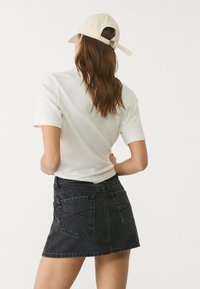 Camicia bianca a maniche corte abbinata a una mini gonna di jeans nera. L'outfit è completato da un cappellino beige, con una cinturino sul retro.