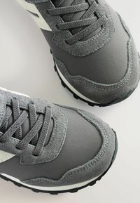 Gray athletic shoes with a mix of suede and mesh materials. Featuring black rubber soles, gray laces, and white accents on the sides.