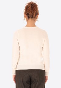 Maglione color crema con collo rotondo, maniche lunghe e orlo a coste. Tessuto morbido, silhouette attillata, indossato con pantaloni a tartan.