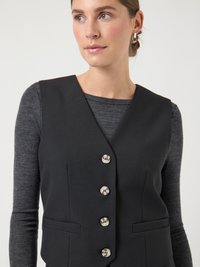 Zwart op maat gemaakt vest met een diepe V-hals, vijf zilveren knopen, twee zijzakken en een gladde textuur, gedragen over een grijs shirt met lange mouwen.