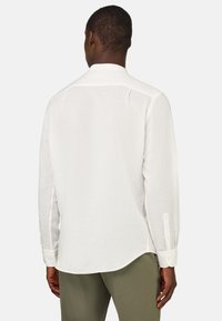 Camicia bianca a maniche lunghe con orlo curvo, polsini abbottonati e vestibilità rilassata. Il tessuto sembra leggero e testurizzato.