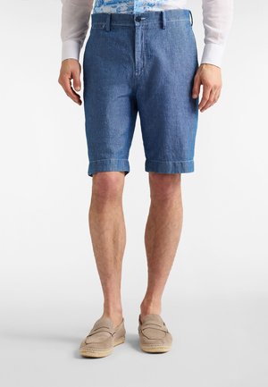 Džínové šortky svetlomodrej farby s vyhrnutými lemami, vybavené zapínaním na gombík a pútkami na opasok. Kombinované s béžovými slip-on topánkami.