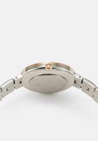 Reloj de pulsera en tono plateado que presenta una caja redonda con un bisel y una corona en tono oro rosa, unido a una pulsera de eslabones metálicos.