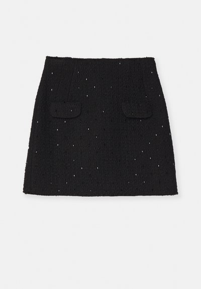 Mini-jupe noire en tissu texturé, dotée d'un motif de petits découpes, avec deux poches avant et une coupe droite.