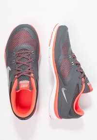 Harmaat ja korallinväriset Nike-juoksukengät, joissa on verkkokangasta, teksturoituja yksityiskohtia ja valkoinen pohja. Kenkäparissa on kontrastiväriset nauhat ja logo.