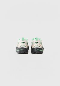 Sneakers feature a white mesh upper with green and black accents, a padded collar, pull tabs, and a textured black sole with green speckles.