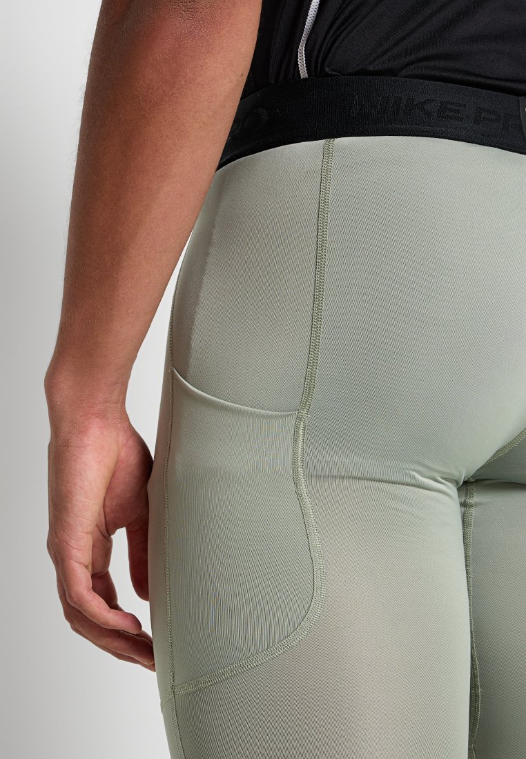 Leggings atléticos de ajuste ceñido, color verde claro, con un acabado texturizado y cinturilla elástica negra con logo. Se ve un bolsillo trasero.