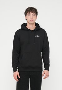 Sweat à capuche noir en mélange de coton avec une poche kangourou, une capuche avec cordon de serrage, et un logo blanc sur la poitrine. Comprend des poignets et un ourlet côtelés.