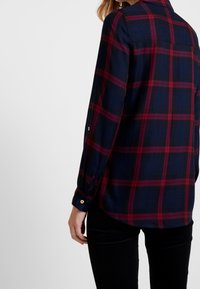 Marineblauwe en rode geruite blouse met lange mouwen, knoopmanchetten en een rugpand. Zacht stoffen met een gestructureerd patroon.