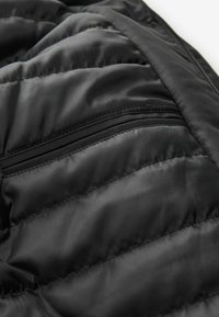 Schwarze Daunenjacke mit gesteppten Abschnitten und einer Reißverschlusstasche; glattes, glänzendes Material mit kontrastierendem mattem Besatz entlang der Kanten.