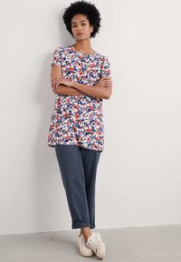 Túnica floral en azul, rojo y blanco con mangas cortas; combinada con pantalones grises de puño enrollado; unas zapatillas crema completan el atuendo.