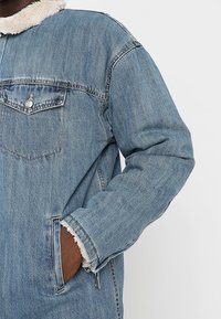 Chaqueta vaquera con un lavado azul claro, con un cuello de piel sintética, bolsillo en el pecho y bolsillos laterales, con puños deshilachados.