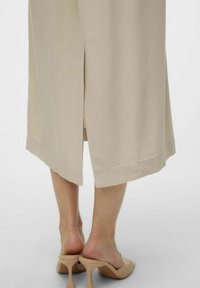 Beige Midi-Kleid mit seitlichem Schlitz und abgestepptem Saum, kombiniert mit nude-farbenen Schuhen mit Blockabsatz, zeichnet sich durch eine glatte Textur und ein minimalistisches Design aus.