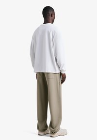 Bela majica z dolgimi rokavi, sproščen kroj, kombinirana z bež širokimi hlačami. Čevlji so svetle barve z nežnimi teksturami in oblikovnimi poudarki.