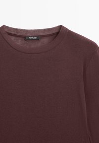Gros plan sur un t-shirt à manches longues col rond couleur bordeaux avec une étiquette Massimo Dutti à l'intérieur du col, fabriqué au Portugal.