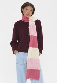 Strikket tørklæde i pink, creme og vinrød med stribet mønster. Blød tekstur, rektangulær form, båret lagdelt over en mørk sweater.