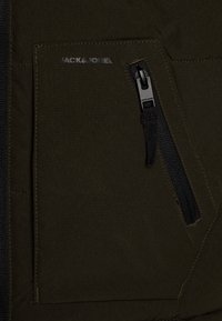 Tessuto della giacca verde oliva con una tasca con zip, caratterizzata da una zip nera e dettagli di cucitura. Logo "JACK & JONES" in argento sulla tasca.