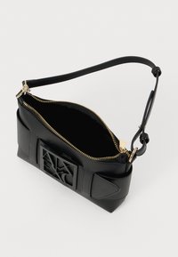 Black leather handbag with gold zipper, adjustable strap, and raised Armani Exchange logo on front, shown open and empty.