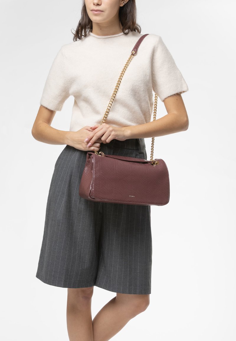 Borsa bordeaux realizzata in pelle texturizzata, con catena dorata e design strutturato, posizionata su uno sfondo chiaro.