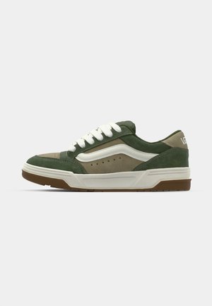 Zapatilla de ante verde y beige con cordones blancos, suela de goma y detalles perforados en el lateral para ventilación.