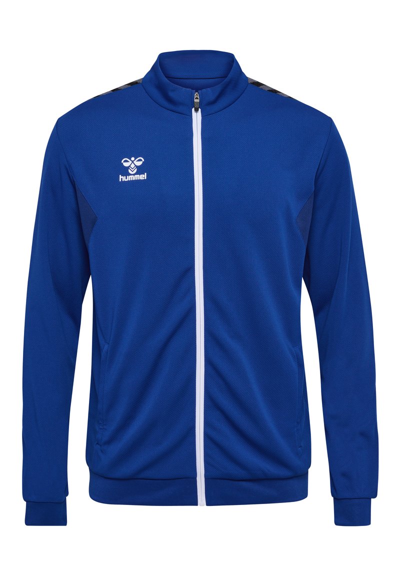 Veste zippée bleue en tissu léger avec poches latérales, panneaux sombres contrastants et fermeture éclair blanche. Dotée d'un logo sur le haut à gauche.