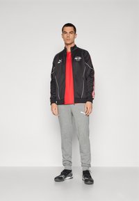 Svart löpjacka med vita detaljer och logo, ljusröd t-shirt, gråa sweatpants och svarta träningsskor. Enkel, sportig design.