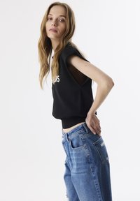 Sudadera negra recortada con cuello redondo y mangas cortas, combinada con unos pantalones vaqueros de denim de tiro alto, de color azul claro y desgastados.