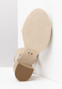 Sandalia de tacón alto beige con suela texturizada, incluyendo detalles de la marca y del tamaño; las correas son lisas con un diseño minimalista.