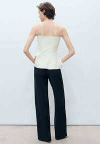 Top bez ramínek v krémové barvě s přiléhavým korzetem a peplum detailem, v kombinaci se volnými černými kalhotami. Hladká textilie, neutrální barvy.
